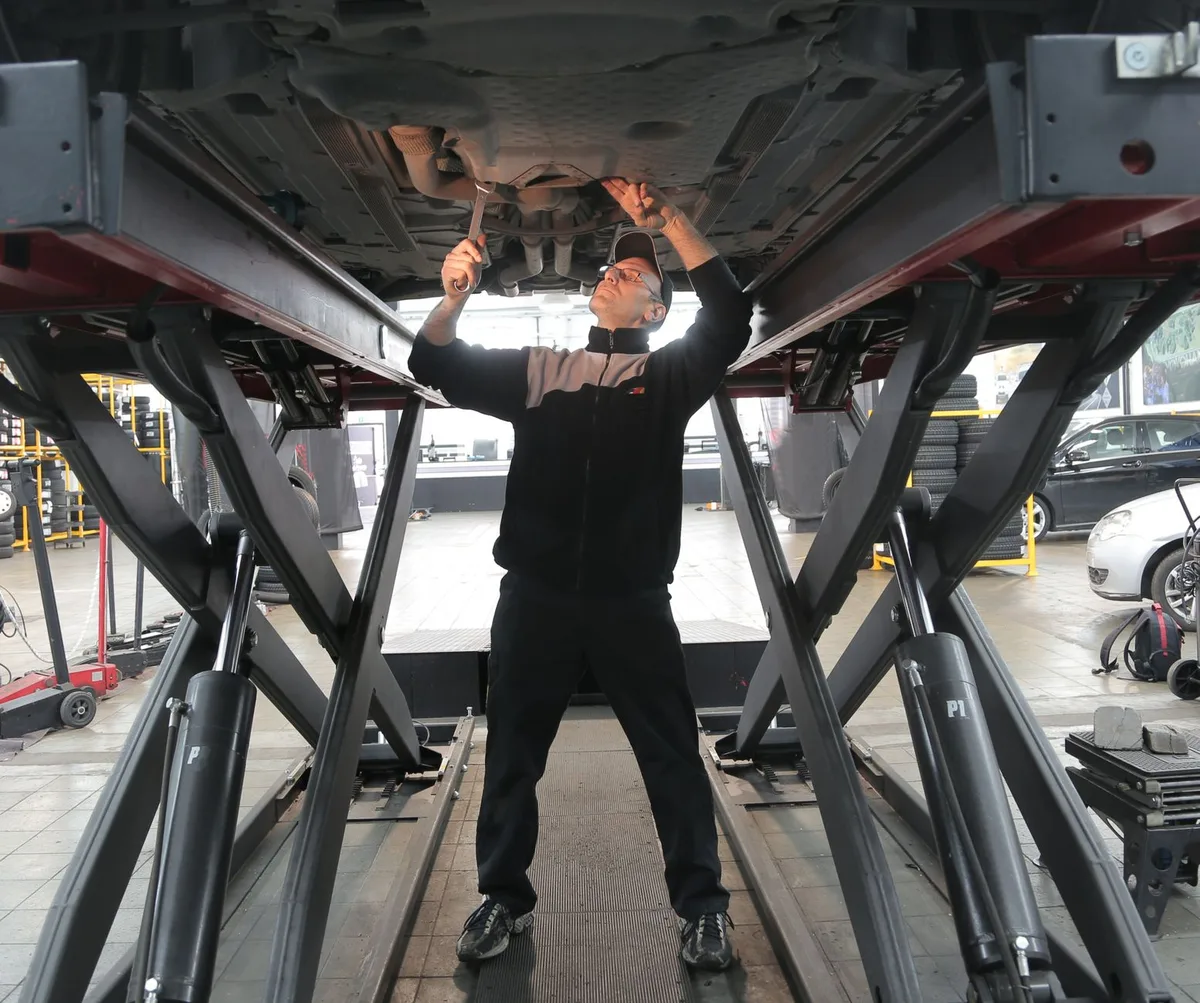 Mecânico trabalhando sob um carro na oficina, inspecionando a parte inferior do veículo