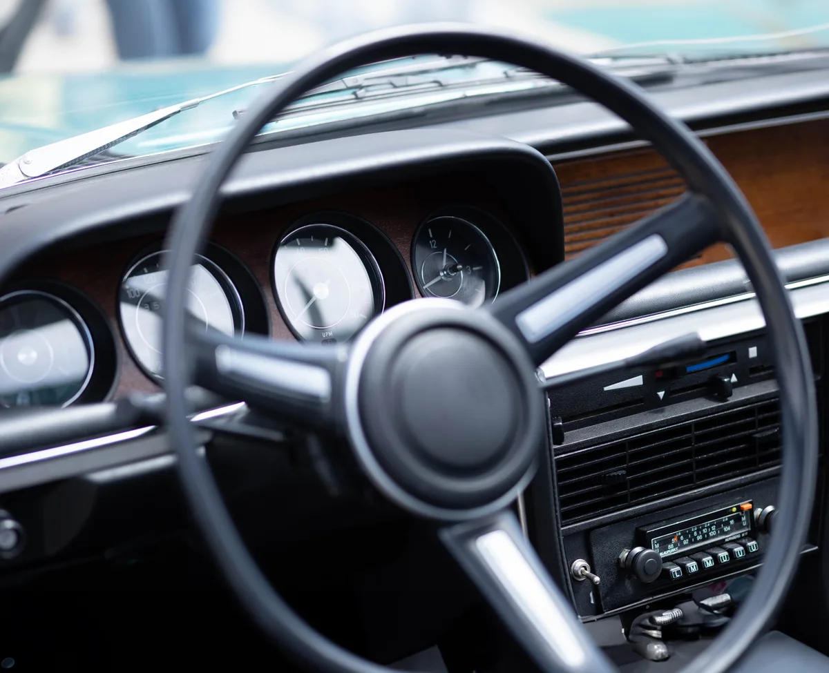 Painel de carro com volante à mostra, instrumentos visíveis ao fundo